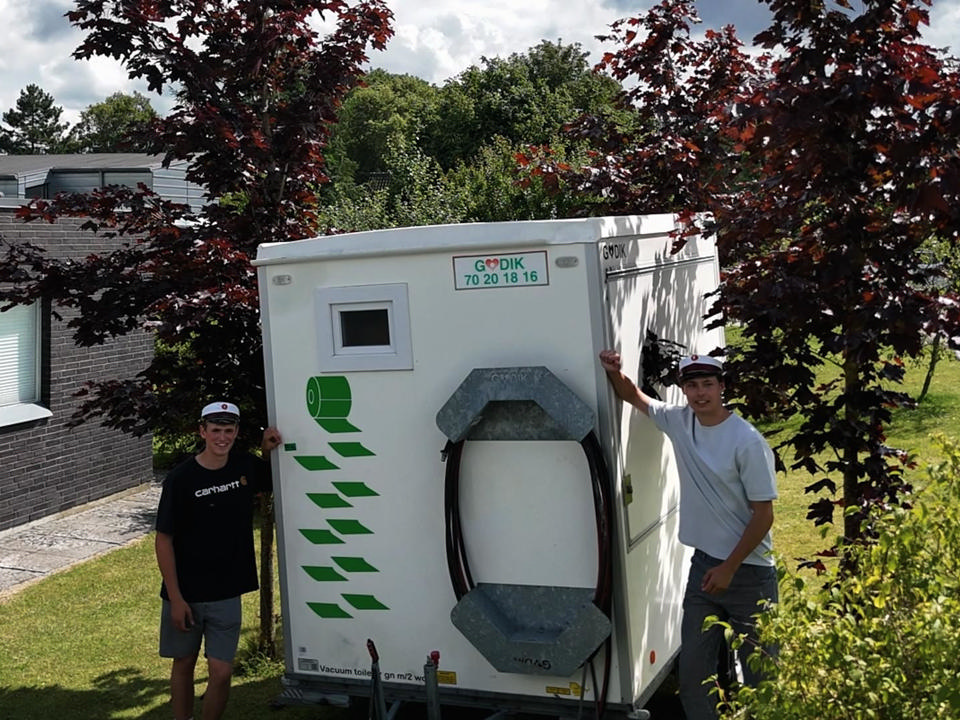 To unge studenter foran en Godik vaacum toiletvogn, lejet til studenterfest i haven